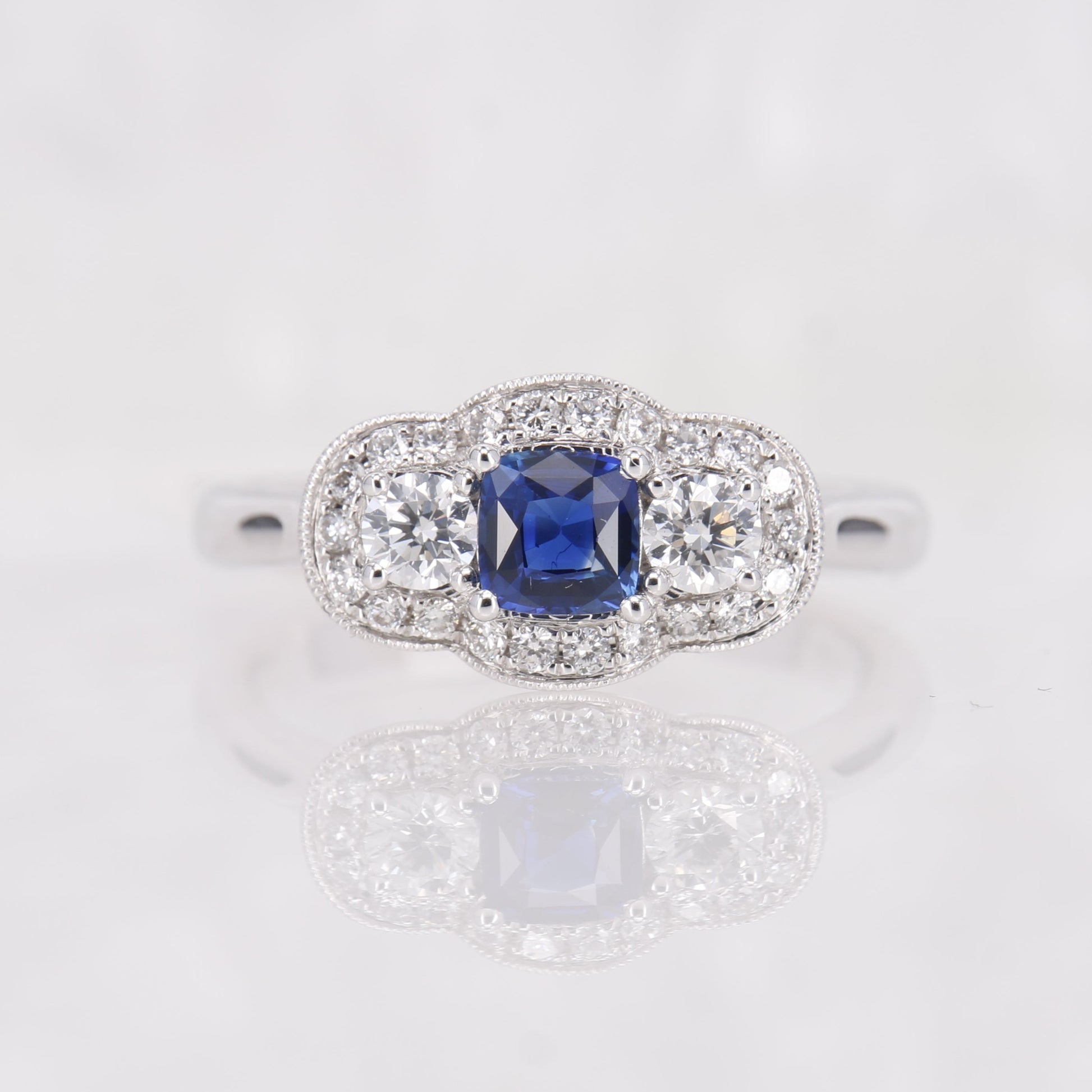 Sapphire and Diamond 3 stone ring. Cushion cut sapphire with round brilliant cut diamonds in a halo of diamonds. Set in 18ct White Gold. 