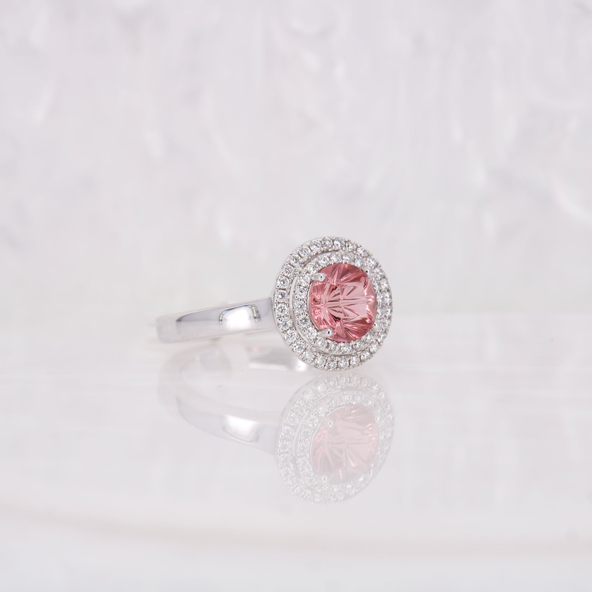 Pink Tourmaline and Diamond ring. Featuring a striking faceted 1.49ct round brilliant cut carved pink tourmaline and complimented by a double halo of diamonds.