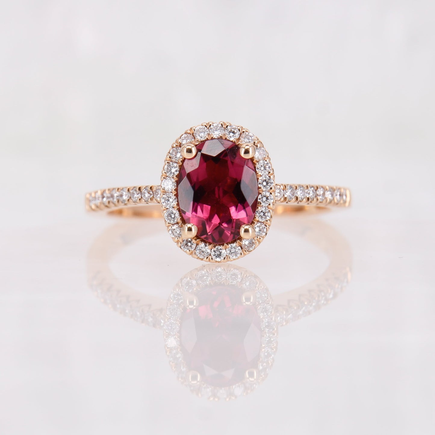 1.07ct Pink Tourmaline Diamond ring. At the centre of the ring is a deep pink oval cut tourmaline. Surrounding the tourmaline is a halo of sparkling diamonds. Adorning the shoulders of the ring are additional diamonds, meticulously set to cascade down the band. Crafted from luxurious 18ct rose gold, the warmed-toned rose gold complements the pink tourmaline and diamonds perfectly.