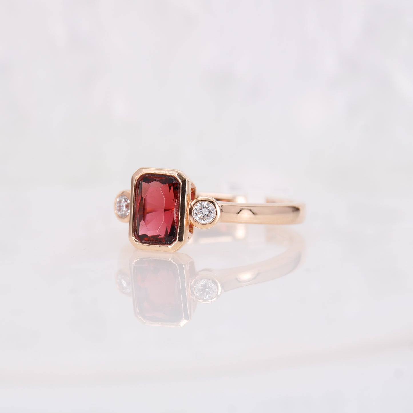 Rubellite and Diamond Ring. Crafted in luxurious 18ct rose gold, this ring features a central radiant rubellite, complemented by two sparkling round brilliant cut diamonds.